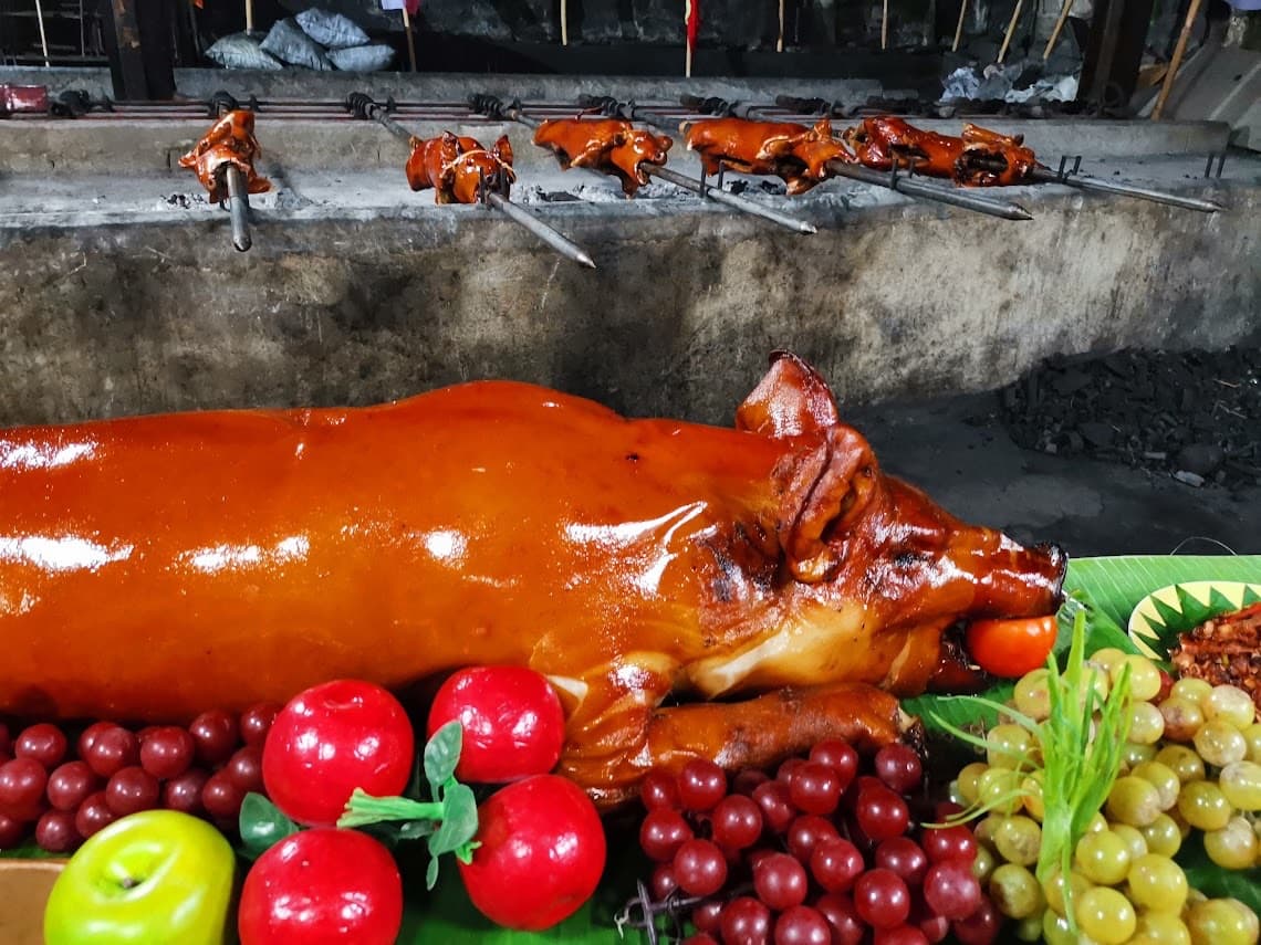 Whole roasted lechon on a fruit platter with more lechon turning on spits behind